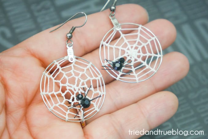 Hand holding hoop earrings with spider web crocheted in them.