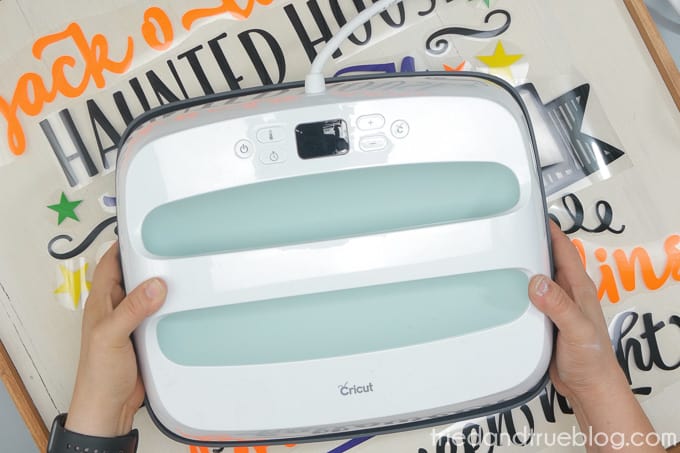 Hand holding Cricut EasyPress in front of wood board.