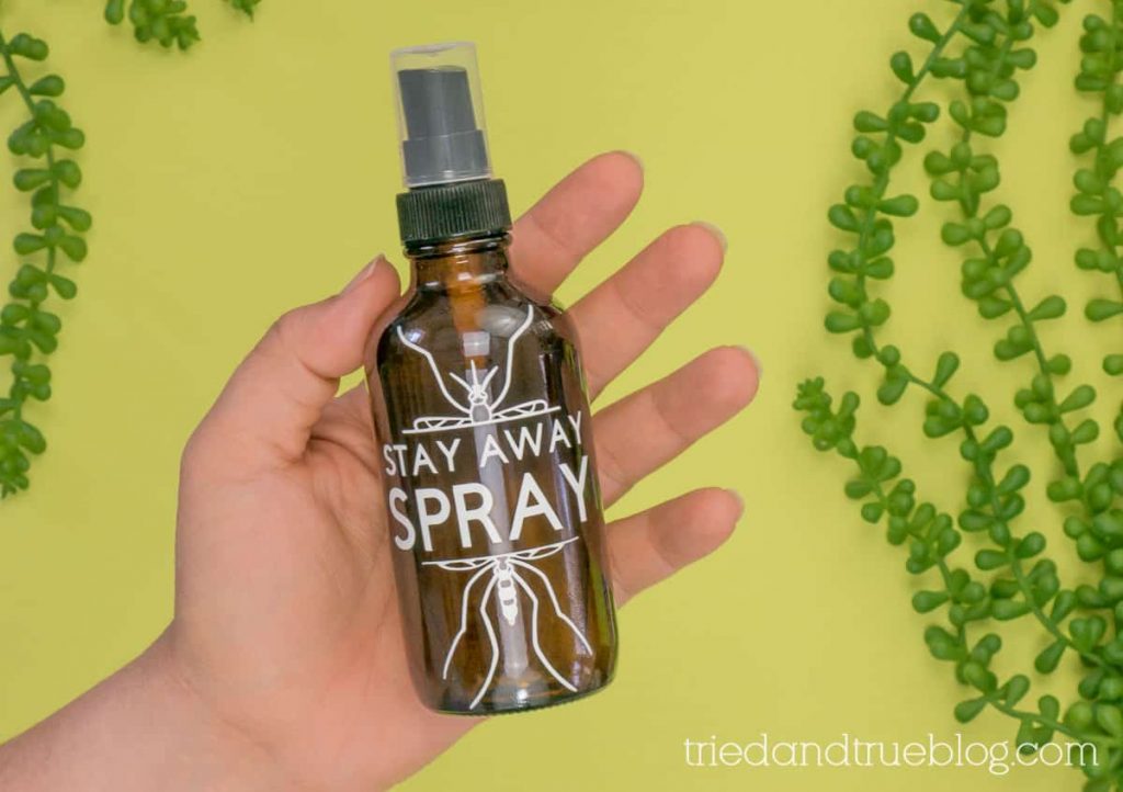 Hand holding a bottle of Homemade Mosquito Repellent over green background.