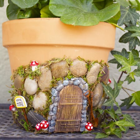 A terracotta flower pot decorated with stones, moss, and miniature figurines to resemble a fairy house.