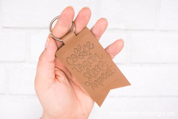 Hand holding a debossed leather keychain that says "Coffe Teach Sleep Repeat."