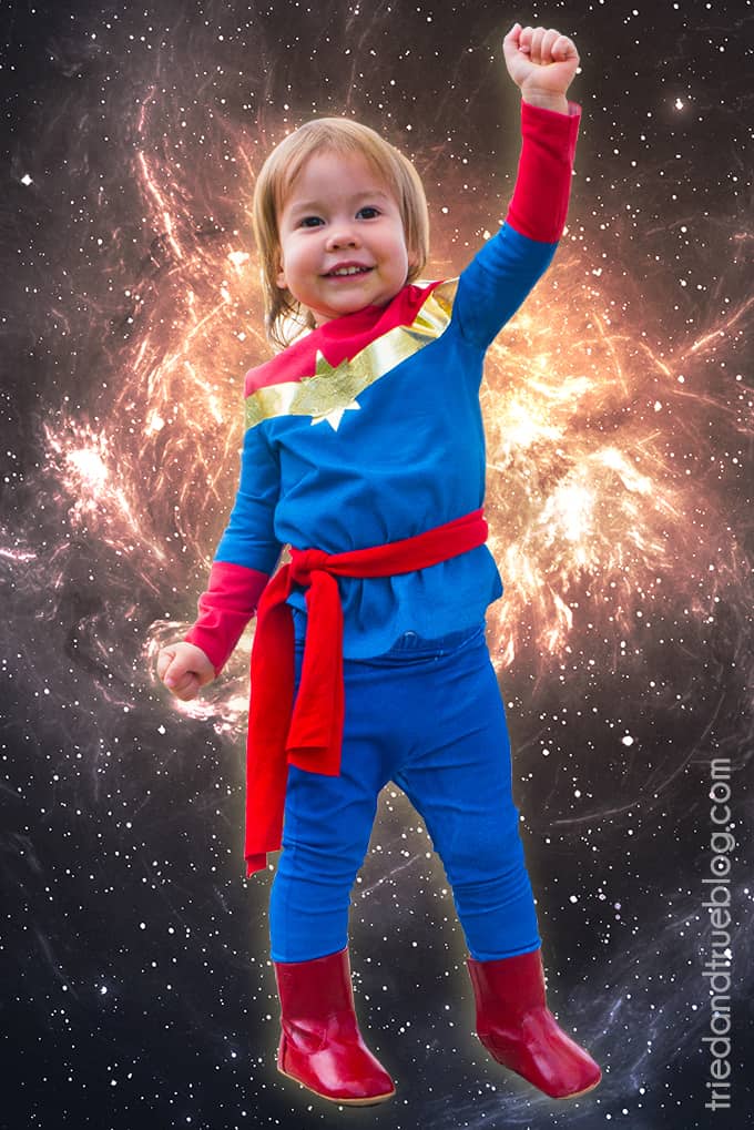 Toddler wearing No-Sew Captain Marvel Toddler Costume photoshopped in front of space background.