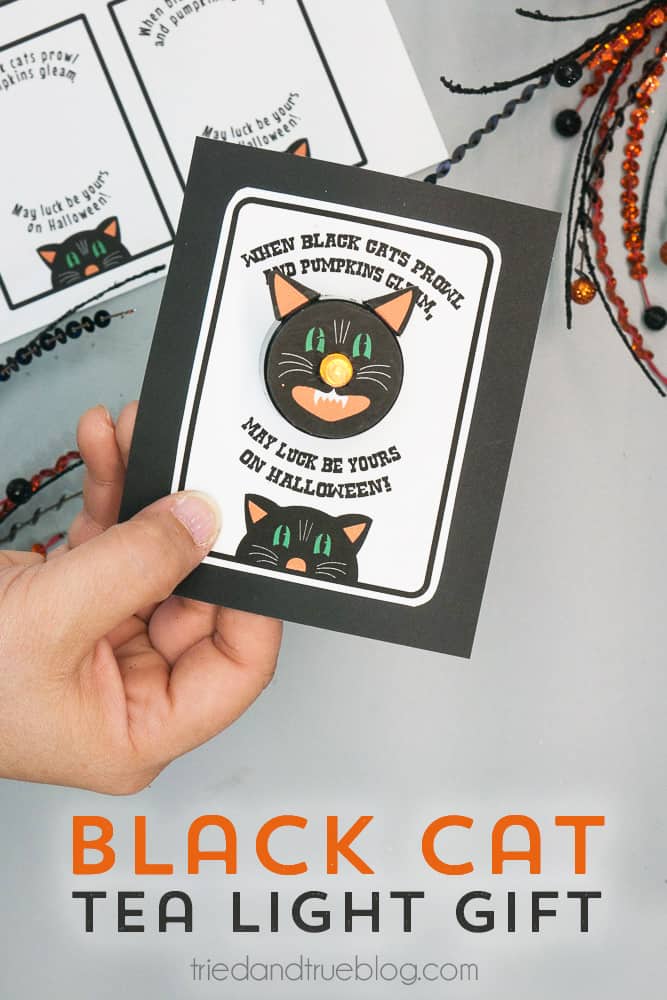Hand holding a card with Black Cat Tea Light Halloween Gift and words "When black cats prowl and pumpkins gleam, may luck be yours on Halloween!"