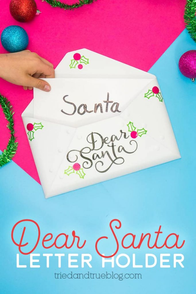 Child's hand inserting letter into a metal Santa Letter Holder that says "Dear Santa" in the front.