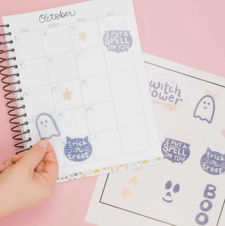 Hand placing cute Halloween free stickers in planner