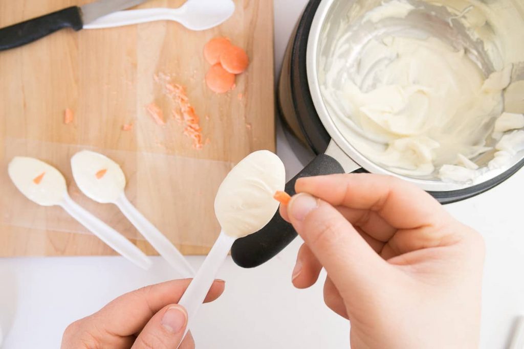 Hand holding white spoon with white chocolate.