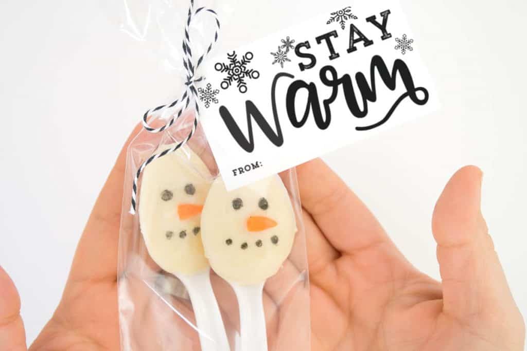 Hands holding snowman hot chocolate stirrers with the "Stay Warm" Gift Tags.