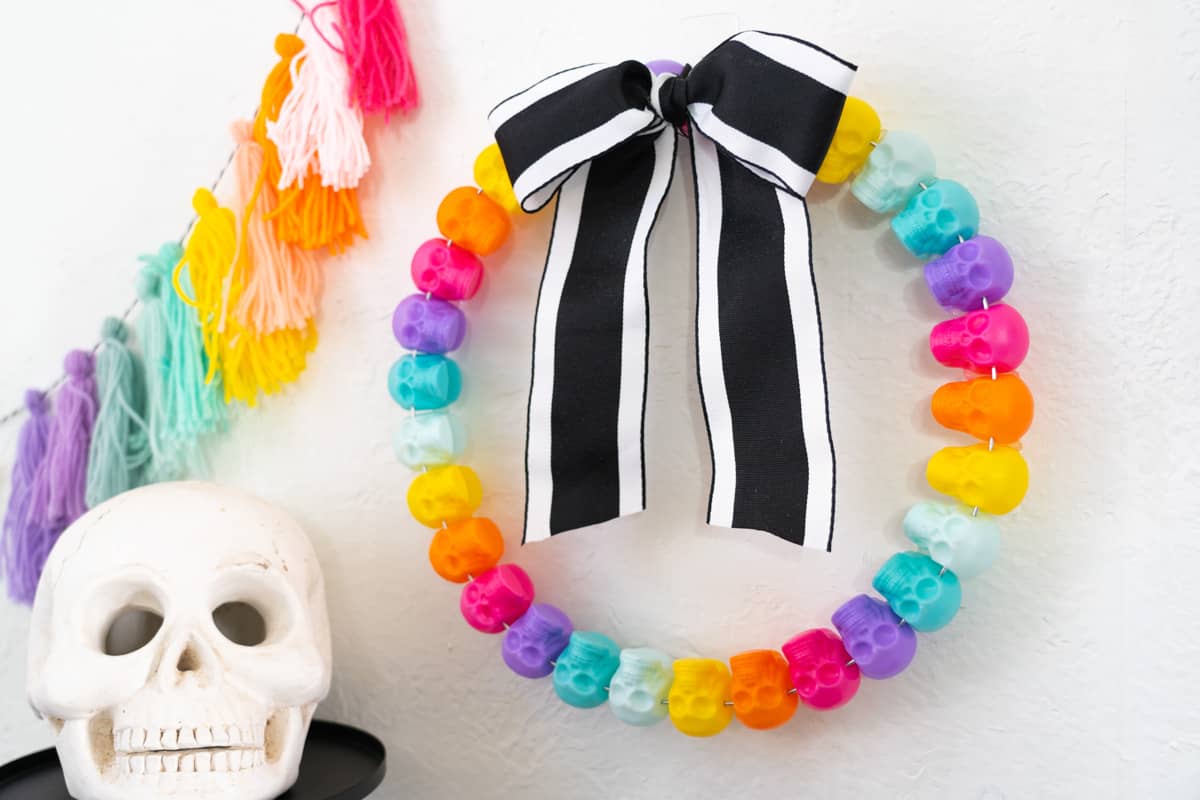 Colorful Halloween Wreath craft made of colorful skulls on a white wall with Halloween decor surrounding it.