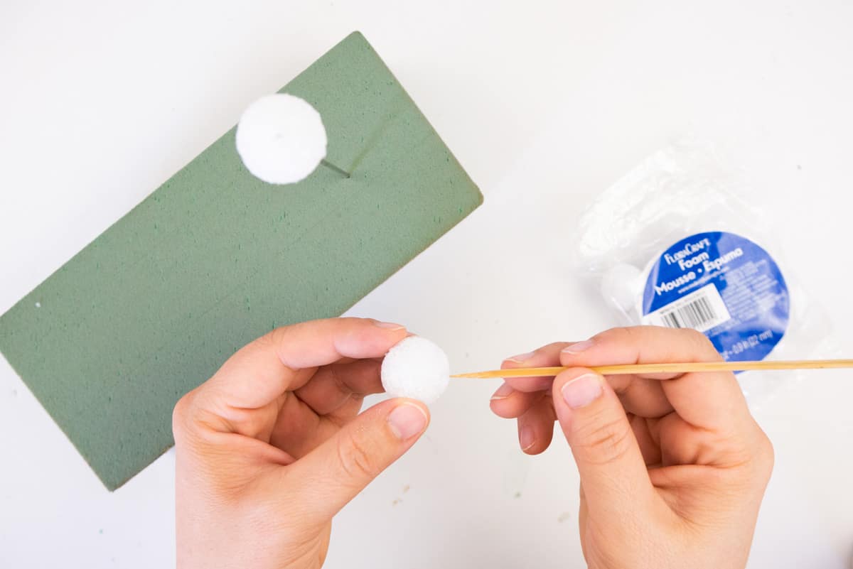 Hand pushing wood skewer into styrofoam ball.