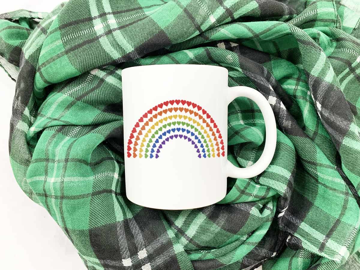 White mug on a green scarf with a rainbow design made of hearts