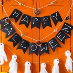 Happy halloween banner with ghosts and leaves on an orange wall.