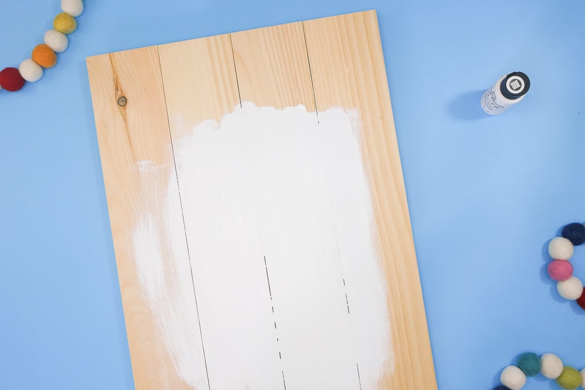 A wooden board with paint and pom poms on it.