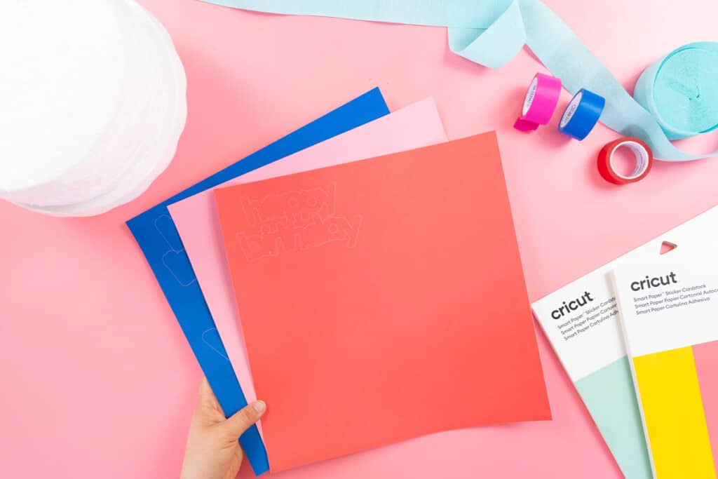 A person holding a Cricut material supplies on a pink background.