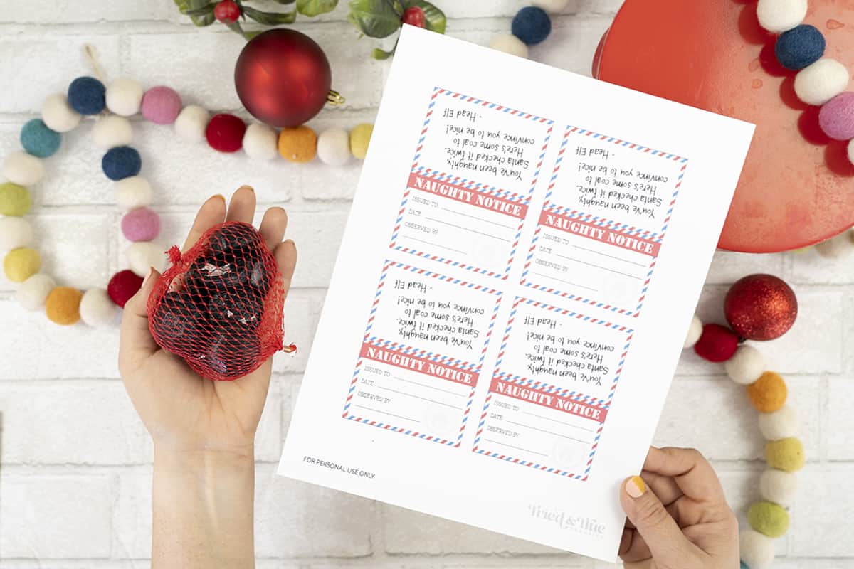 A hand is holding up a Naughty Notice printable christmas gift tag.