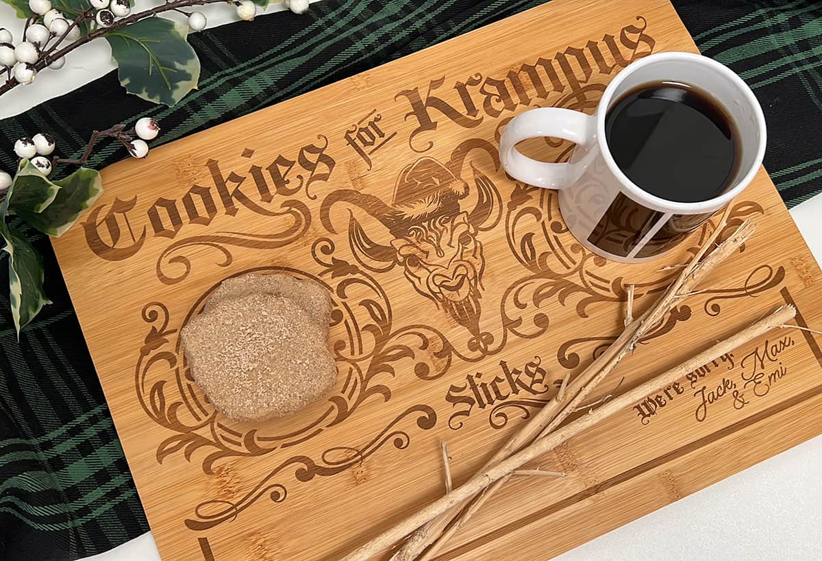 A "Cookies for Krampus" wooden cutting board with a cup of coffee and cookies.