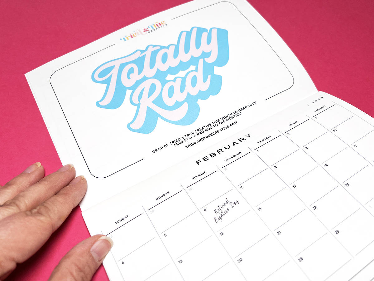 A person holding up a T&TC Free SVG calendar with the word totally rad on it.