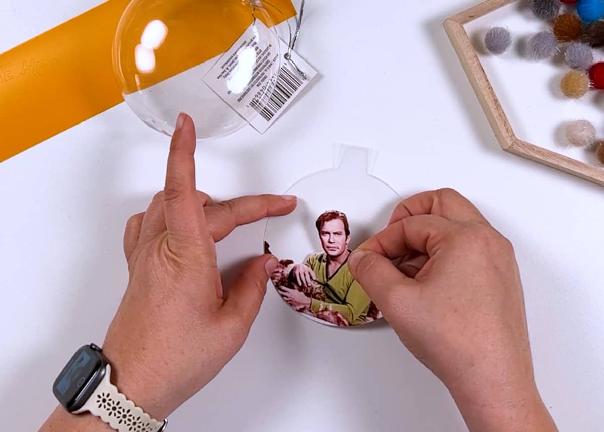 A person is putting a photo into a glass ornament.