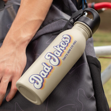 A beige water bottle with the phrase "Dad Jokes: That’s How Eye Roll" printed on it is attached to a gray backpack. A person's hand rests on the backpack.